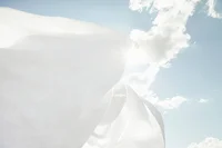 White fabric billowing in the wind against a blue sky with clouds.